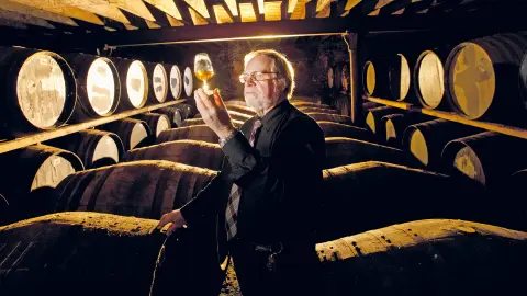 Älterer Mann im Keller einer Whisky-Destillerie mit Holzfässern-placeholder